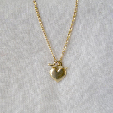 Gold necklace with a heart pendant on a light gray background
