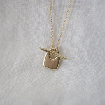 Gold necklace with a unique pendant on a light gray fabric background