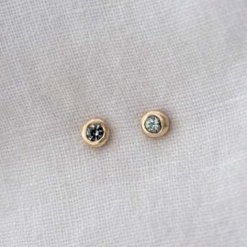 Pair of gold earrings with gemstones on a light gray fabric background