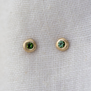 Pair of gold earrings with green gemstones on a light fabric background