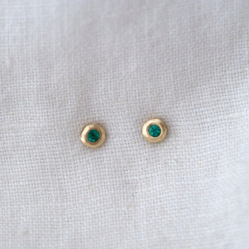 Gold earrings with green gemstones on a white fabric background
