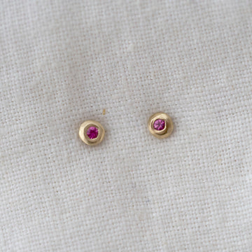 Pair of gold earrings with pink ruby gemstones on a light gray fabric background