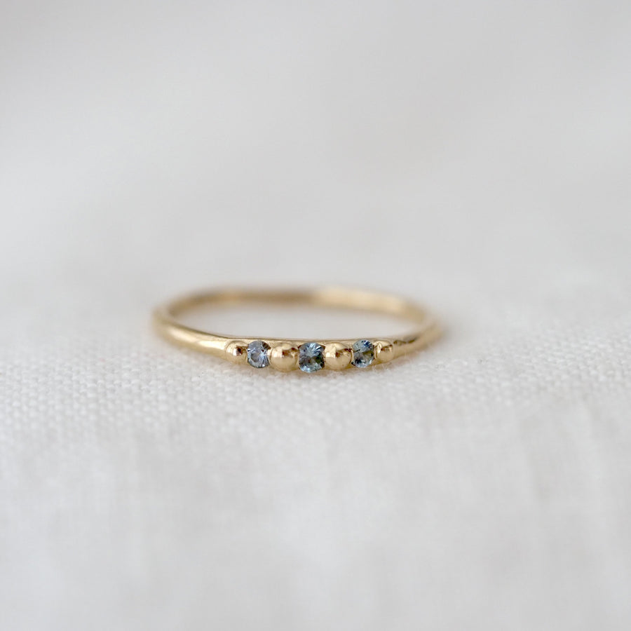 Gold ring with three small blue stones on a white fabric background