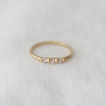 Gold ring with three small white stones on a white fabric background