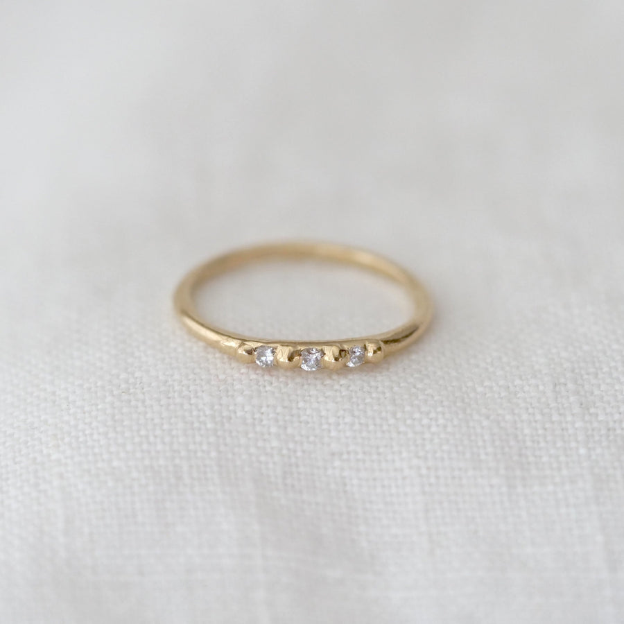 Gold ring with three small white stones on a white fabric background