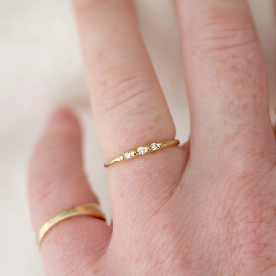 Close-up of a hand wearing two gold rings with a white stone on a light background