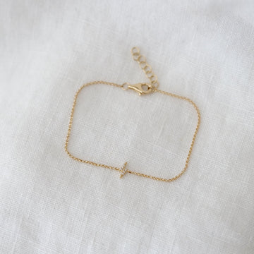 Gold bracelet with a small lightning bolt charm on a white fabric background