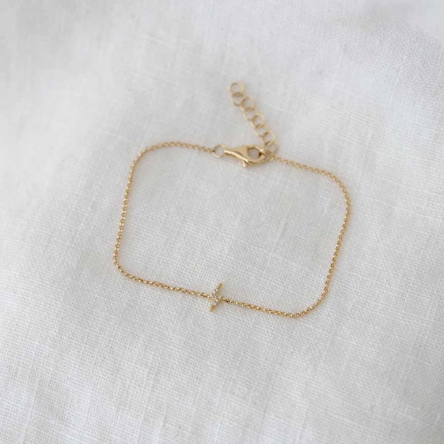 Gold bracelet with a small lightning bolt charm on a white fabric background