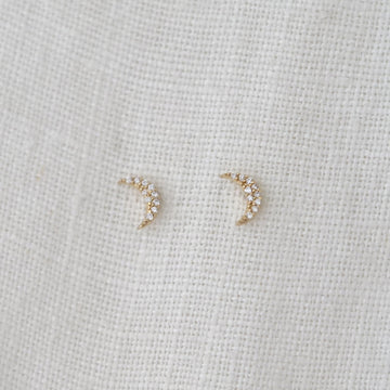 Pair of delicate moon stud earrings on a light fabric background