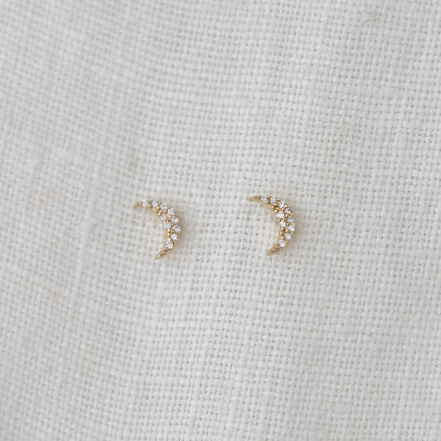 Pair of delicate moon stud earrings on a light fabric background