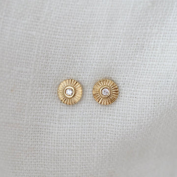 Gold earrings with a central gemstone on a light gray background