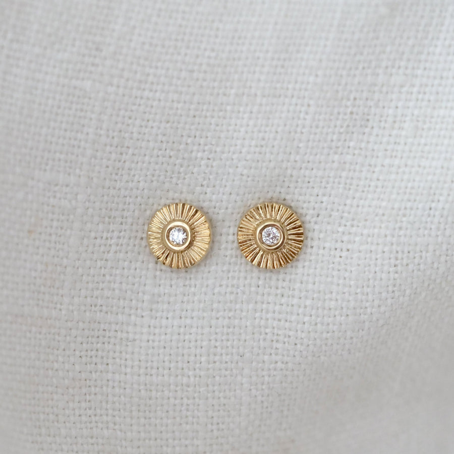 Gold earrings with a central gemstone on a light gray background