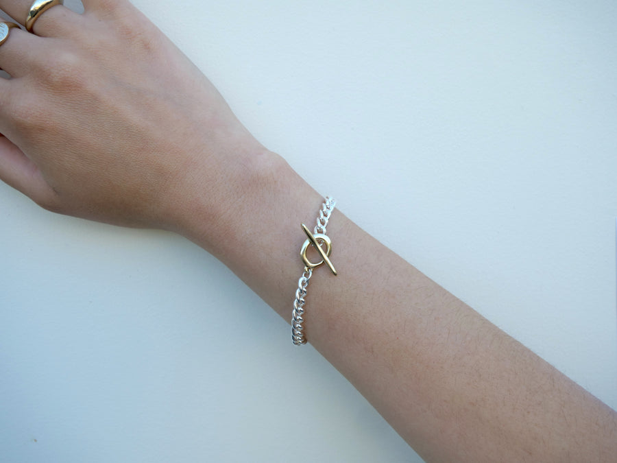 Silver bracelet with a gold clasp on a wrist against a white background