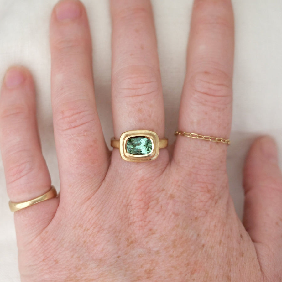 Hand wearing a gold ring with a green gemstone on a white background