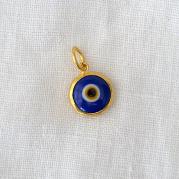Gold pendant with a blue eye design on a white fabric background
