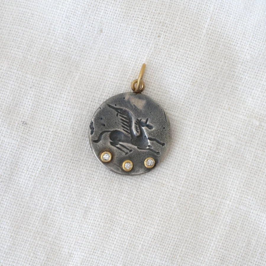 Silver pendant with a bird design and three small stones on a light fabric background