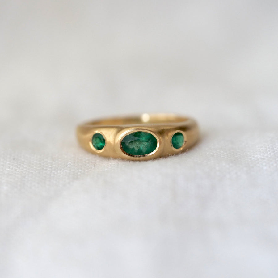 Gold ring with three green gemstones on a white fabric background