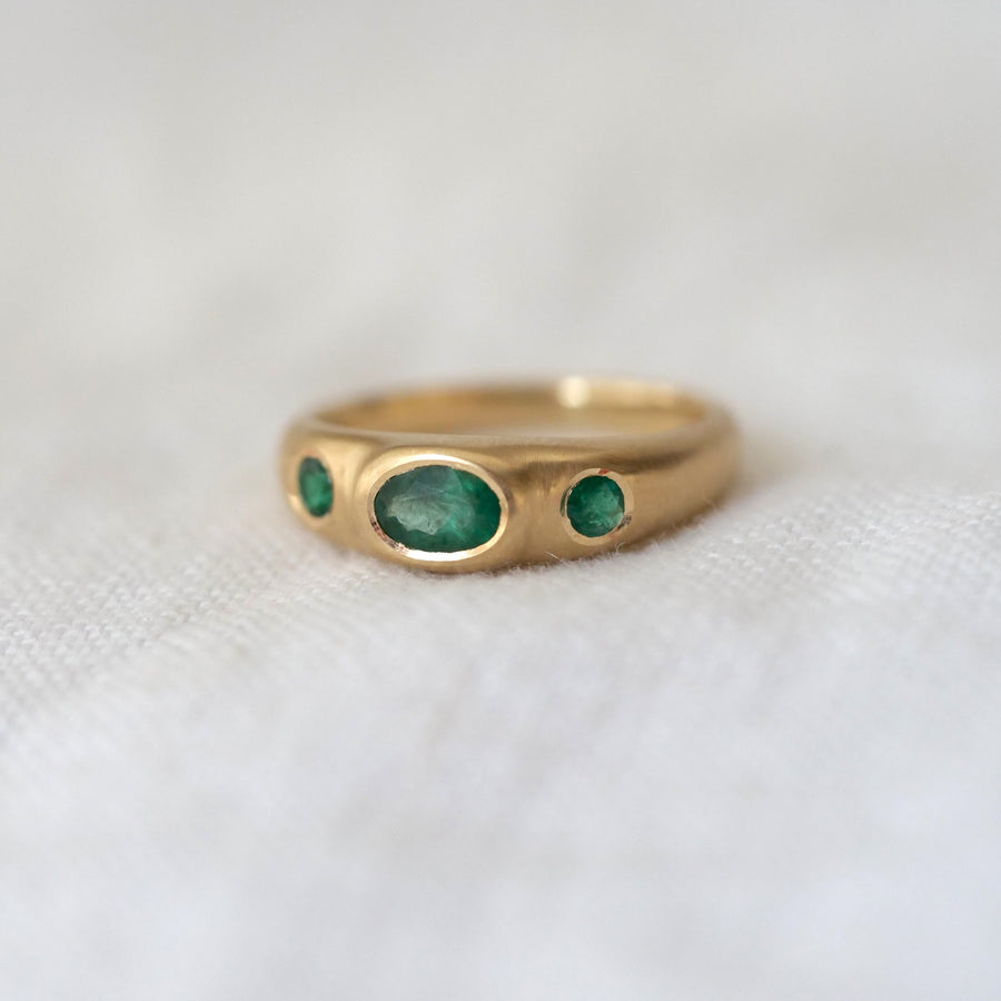 Gold ring with three green gemstones on a white fabric background