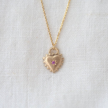 Gold heart-shaped necklace with a pink gemstone on a light gray background
