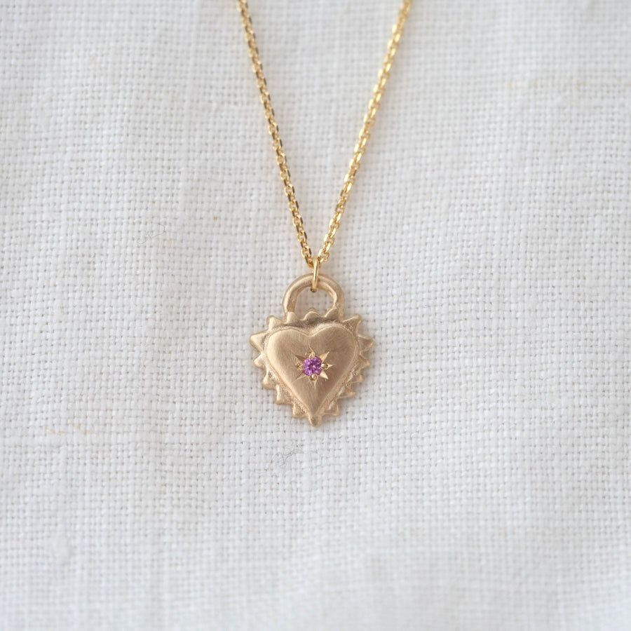Gold heart-shaped necklace with a pink gemstone on a light gray background
