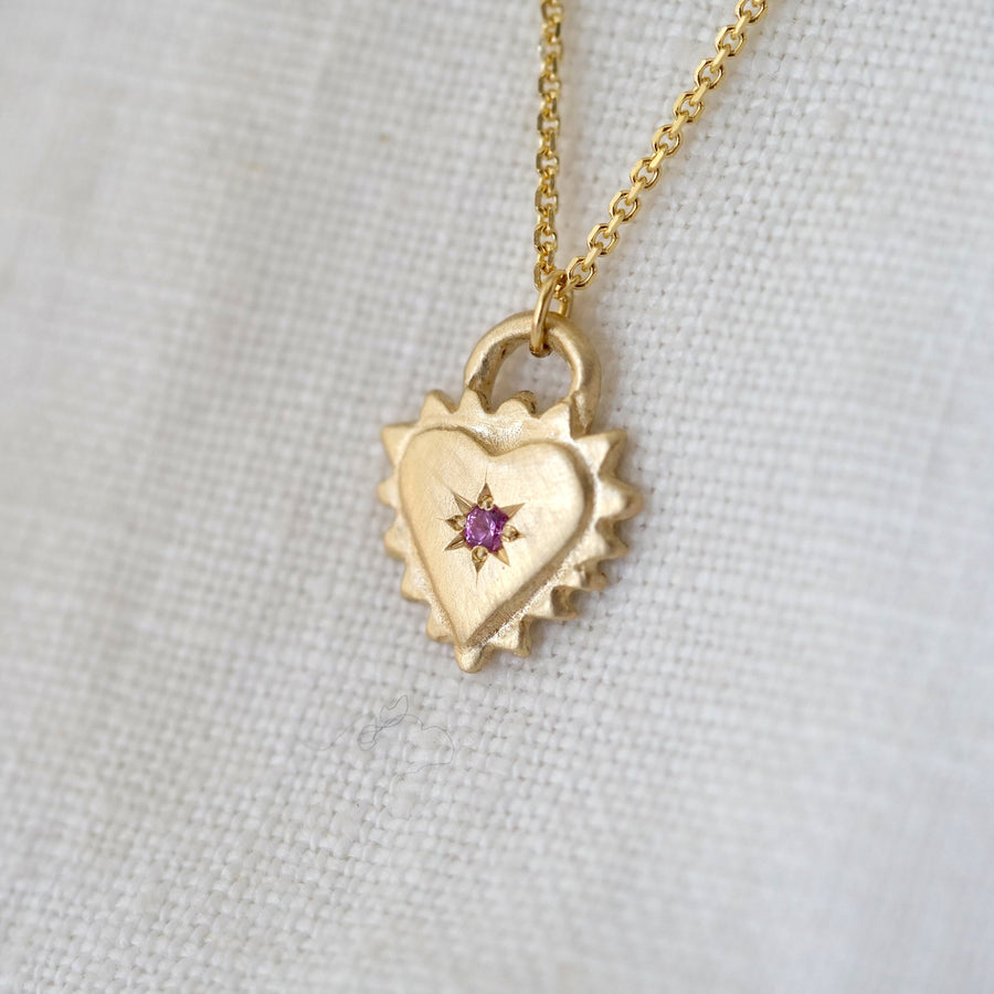 Gold heart-shaped necklace with a pink gemstone on a light gray background