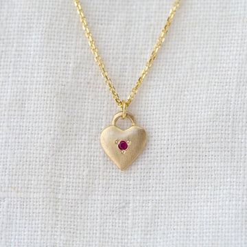 Gold heart-shaped necklace with a red gemstone on a light gray background