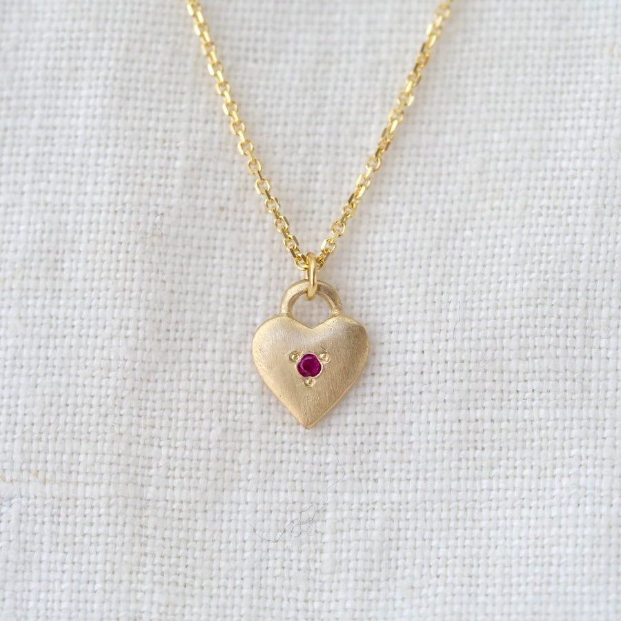 Gold heart-shaped necklace with a red gemstone on a light gray background