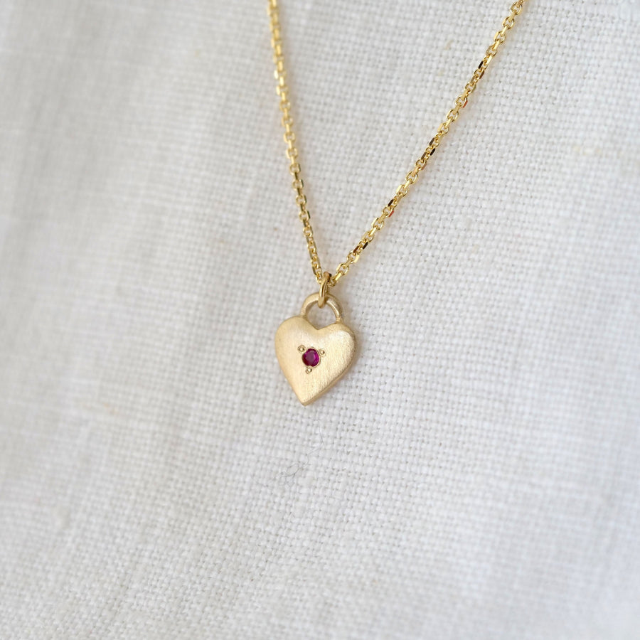 Gold heart-shaped necklace with a red gemstone on a light gray background