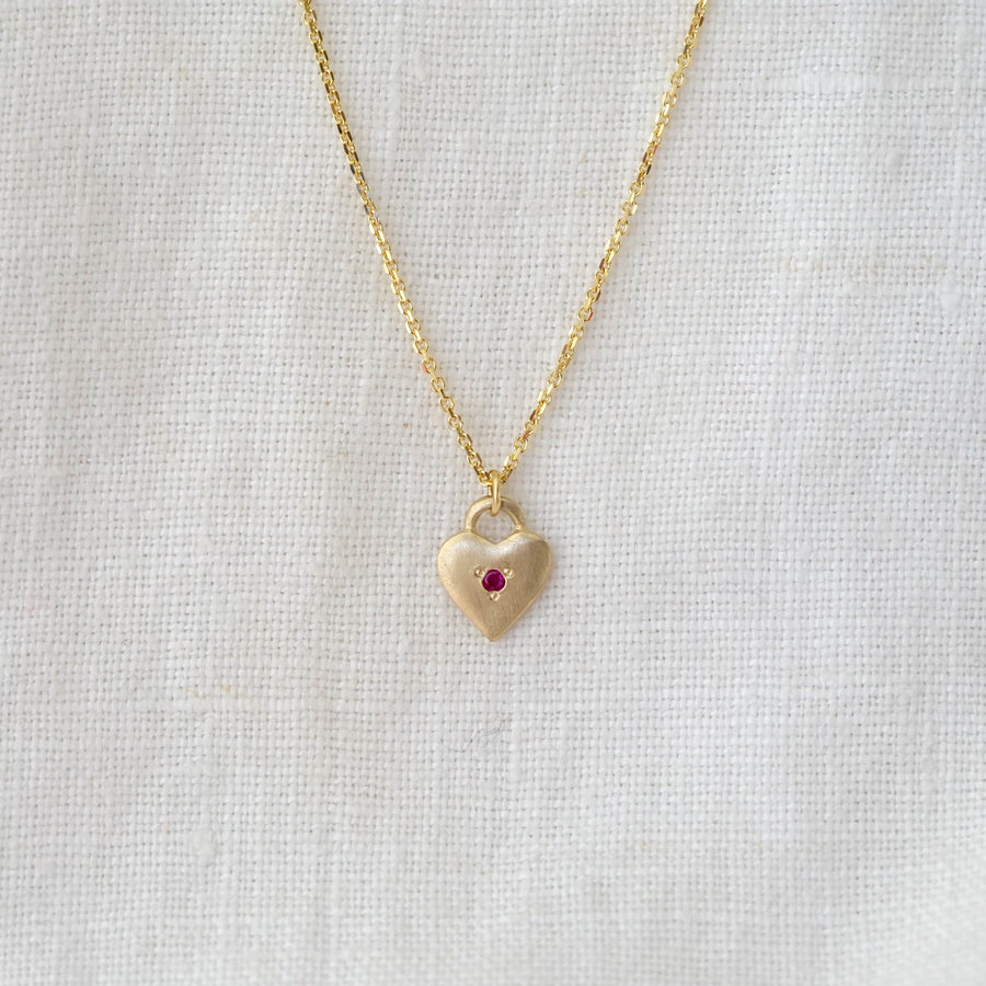 Gold heart-shaped pendant necklace with a red gemstone on a light gray background