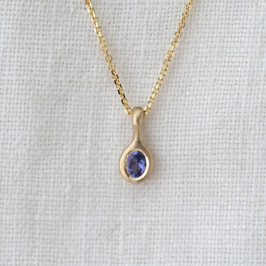 Gold necklace with a pendant featuring a blue gemstone on a light gray background