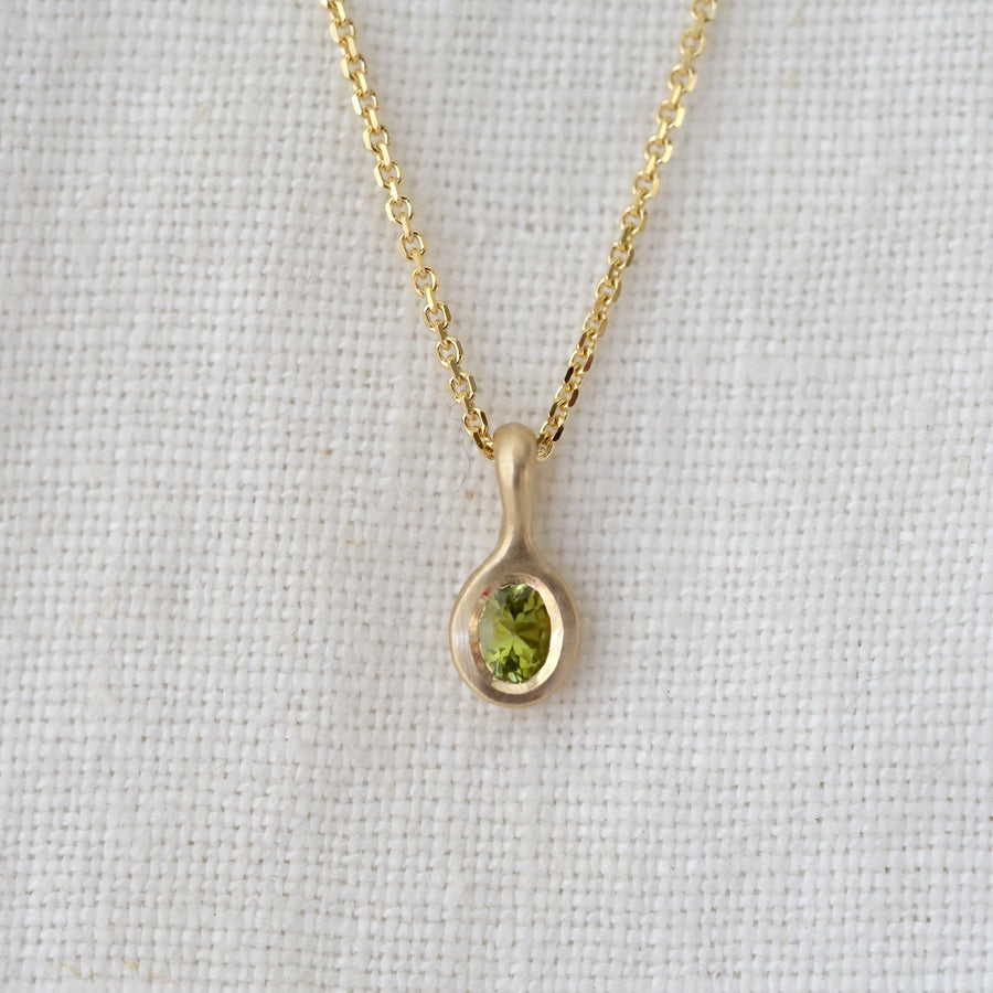 Gold necklace with a green gemstone pendant on a light gray background