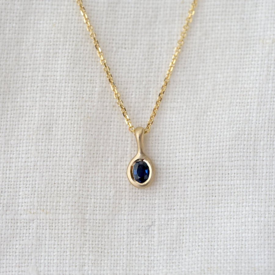 Gold necklace with a blue gemstone pendant on a light gray background