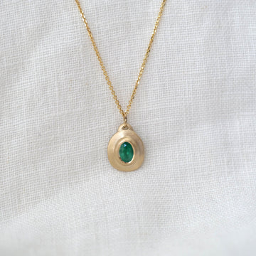 Gold necklace with a green gemstone pendant on a white fabric background