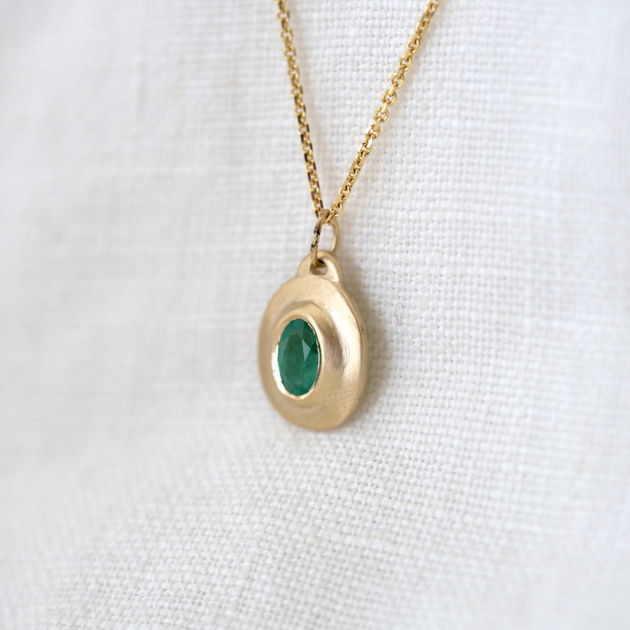 Gold necklace with a green gemstone pendant on a white fabric background