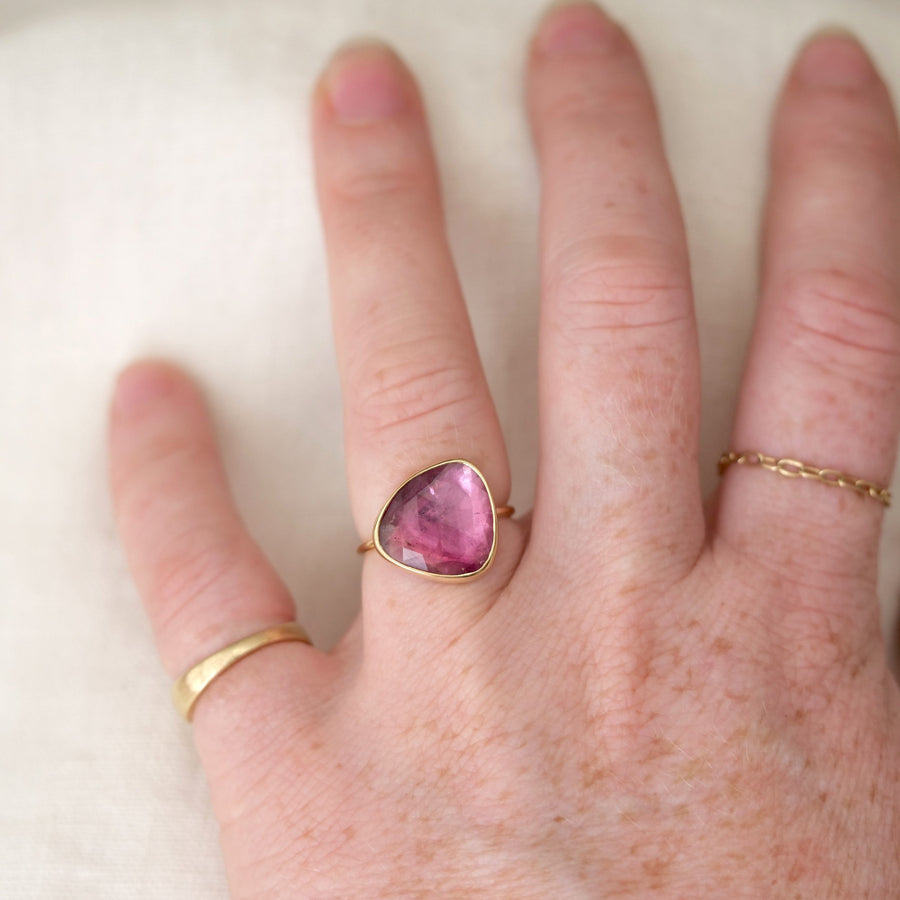 Hand wearing a ring with a pink gemstone on a white background