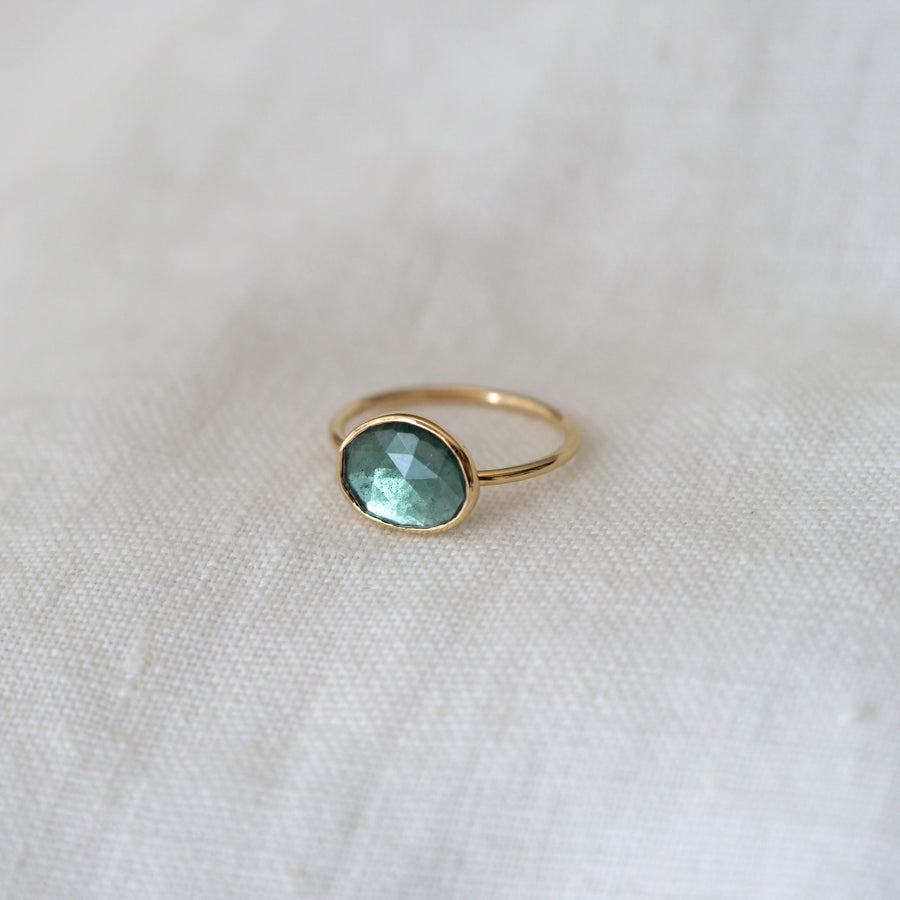 Gold ring with a green gemstone on a white fabric background