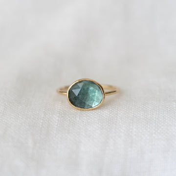 Gold ring with a green gemstone on a white fabric background
