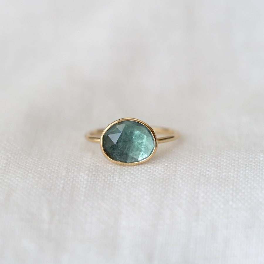 Gold ring with a green gemstone on a white fabric background
