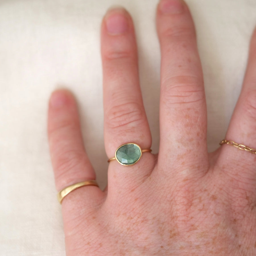 Hand wearing a green gemstone ring on a white background