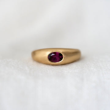 Gold dome ring with a purple red gemstone on a white background
