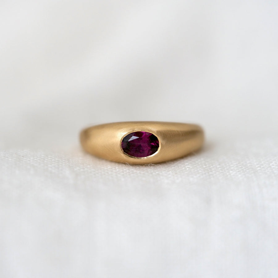 Gold dome ring with a purple red gemstone on a white background