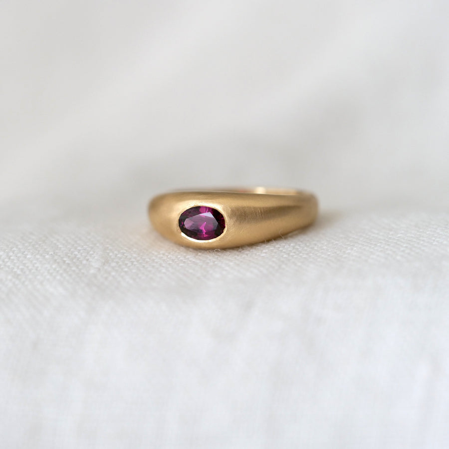 Gold ring with a purple gemstone on a white fabric background