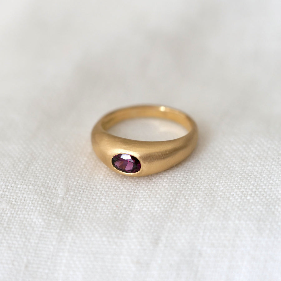 Gold ring with a purple gemstone on a white fabric background