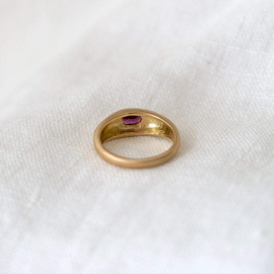 Gold ring with a purple gemstone on a white fabric background