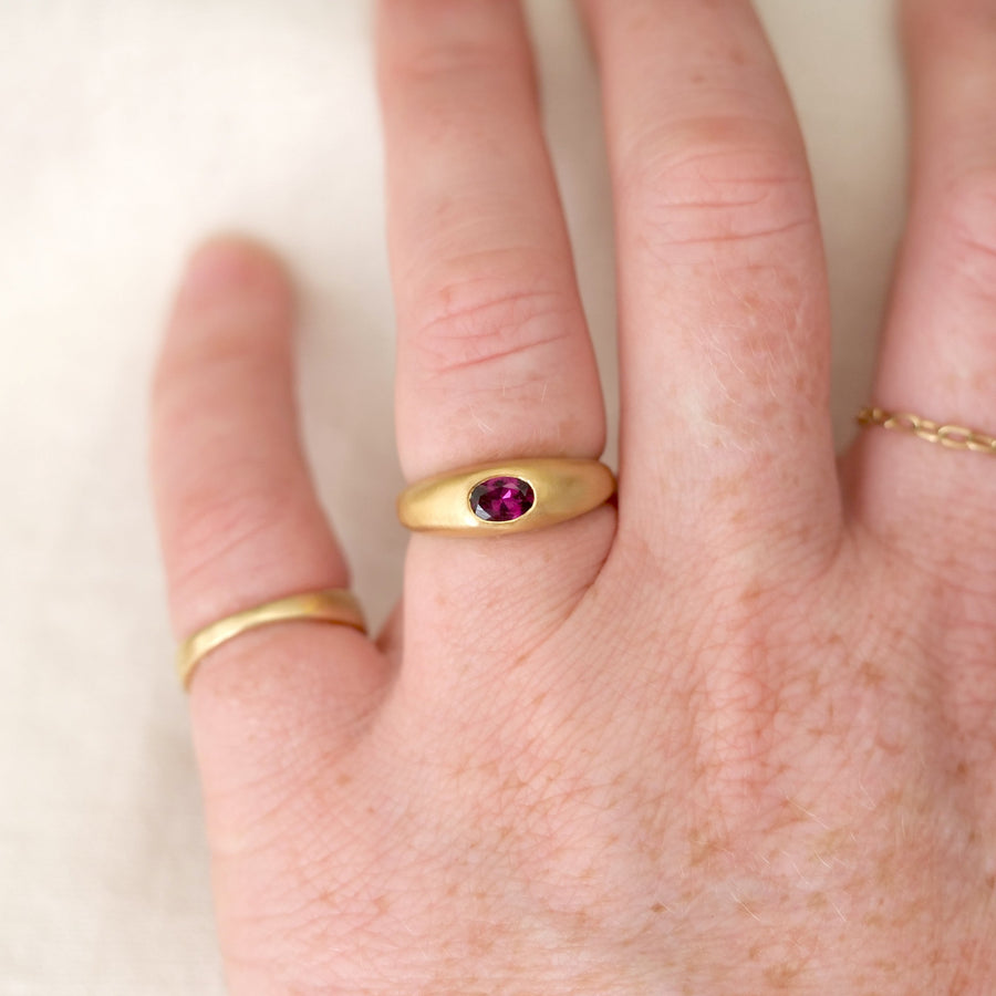 Gold ring with a purple gemstone on a person's finger against a white background