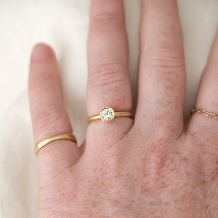 Hand wearing two gold rings with a small diamond on a light background
