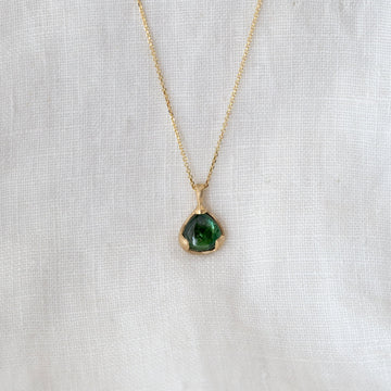 Gold necklace with a green pendant on a white fabric background