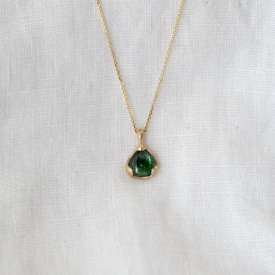 Gold necklace with a green pendant on a white fabric background