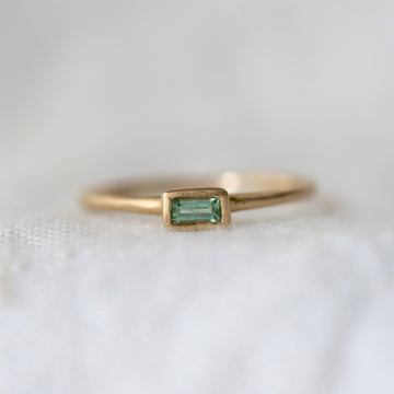 Gold ring with a green baguette gemstone on a white fabric background