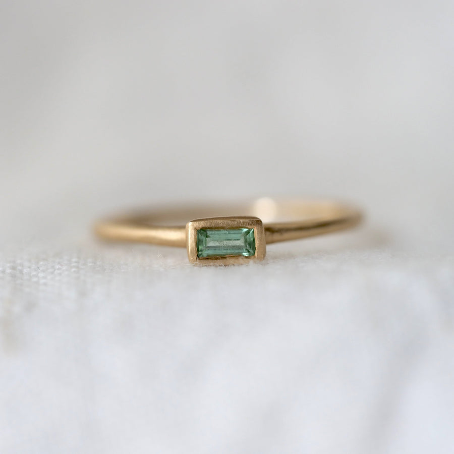 Gold ring with a green baguette gemstone on a white fabric background